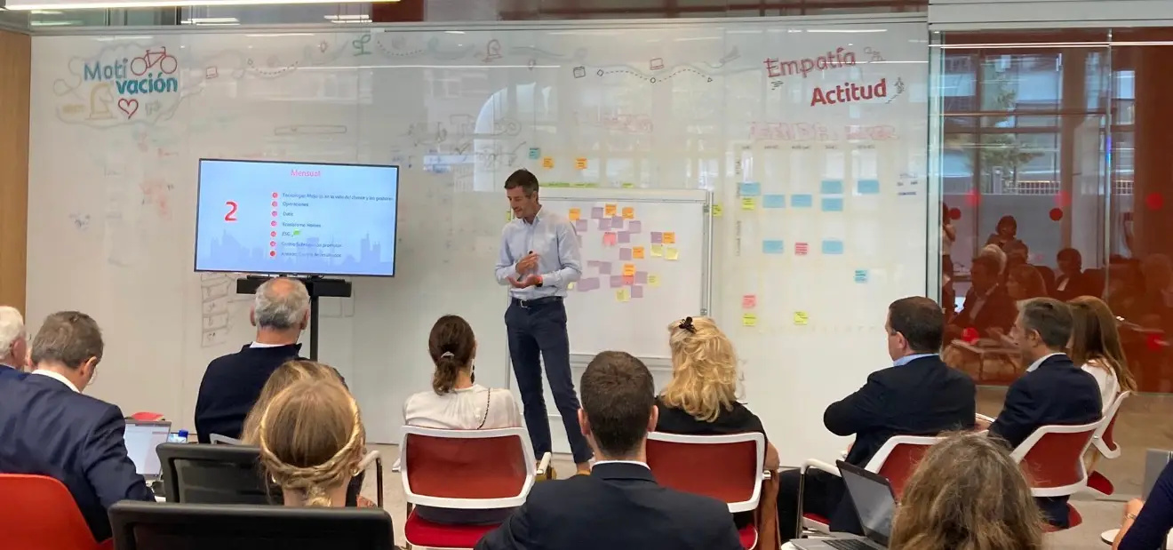 Charly Vaquero explicando ante un grupo en una sala de trabajo, con paneles de notas adhesivas y una pantalla